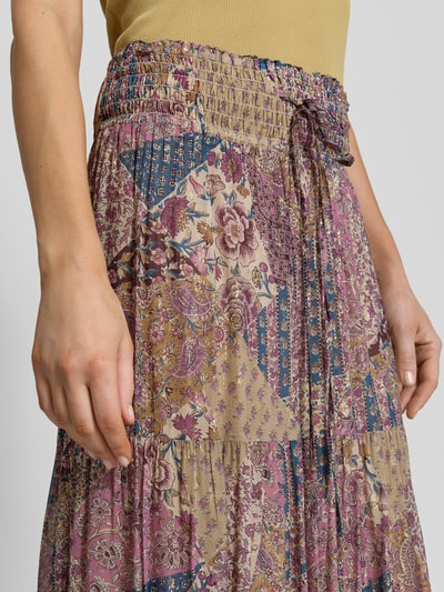 Frauenmodel trägt Maxirock aus Viskose mit Kordelzug Modell 'PITSY' von Bash, florales Patchwork in Lila, Beige und Blau, Nahaufnahme Oberkörper. Reine Viskose, A-Linie, elastischer Bund, Volantsaum, Bundweite 38 cm, Gesamtlänge 90 cm, Größe 36.