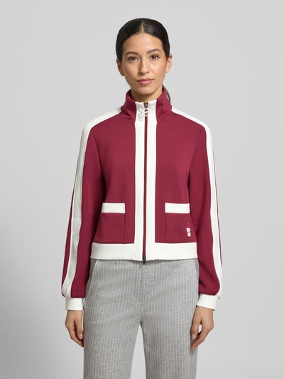 Frauenmodel trägt Regular Fit Sweatjacke mit Stehkragen von Marc Cain in Dunkelrot mit weißen Akzenten, aufgesetzte Taschen, elastischer Material-Mix, Ganzkörperansicht von vorne.