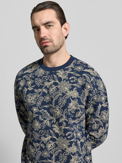 Männermodel trägt sweatshirt im all-over look mit ronde hals von Scotch & Soda, puur katoen, regular fit, blauwe en beige tinten, nahaufnahme oberkörper.