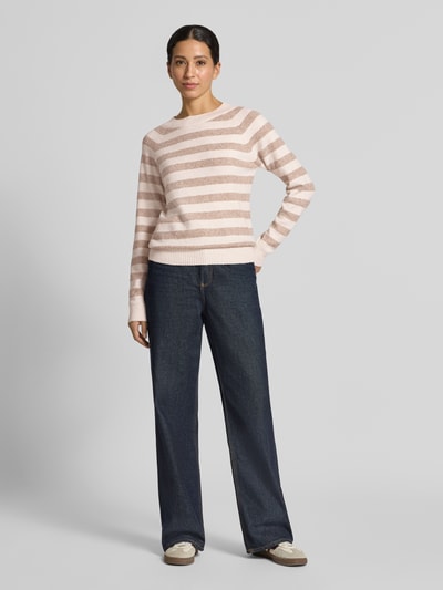 Modelka kobieca nosi Regular Fit sweter z paskami model 'DOFFY' od VERO MODA, beżowe i jasnoróżowe paski, prosty krój, struktura dzianiny, pełny widok od przodu.