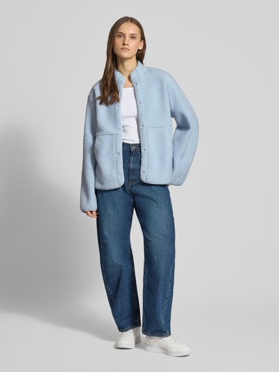 Frauenmodel trägt Relaxed Fit Fleecejacke mit Stehkragen Modell 'VERA' von JJXX aus Teddyfell in Hellblau, Knopfleiste, Eingrifftaschen, Rückenlänge 57 cm, Schulterbreite 41 cm, Brustweite 53 cm, Ärmellänge 54 cm, Ganzkörperansicht von vorne.