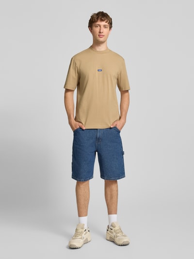 Männermodel trägt Regular Fit T-Shirt aus reiner Baumwolle Modell 'NIEROS' von HUGO in Beige, kombiniert mit blauer Shorts, Herren T-Shirt von HUGO Blue, Ganzkörperansicht von vorne