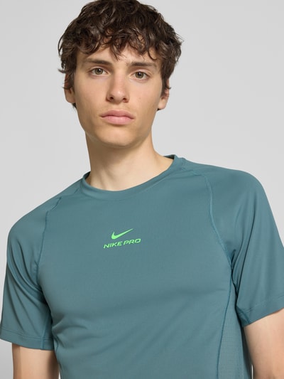 Männermodel trägt T-Shirt mit Logo-Print und Raglanärmeln von NIKE TRAINING in Blaugrün, gerader Schnitt, Nahaufnahme Oberkörper.
