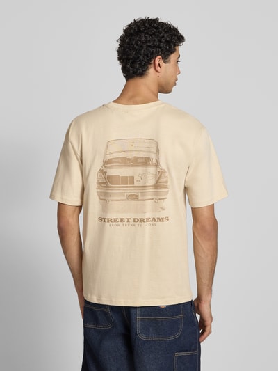 Männermodel trägt Relaxed Fit T-Shirt mit Logo-Stitching von KARL KANI aus reiner Baumwolle in Beige, Rückenlänge 65 cm, Ganzkörperansicht Rückansicht.