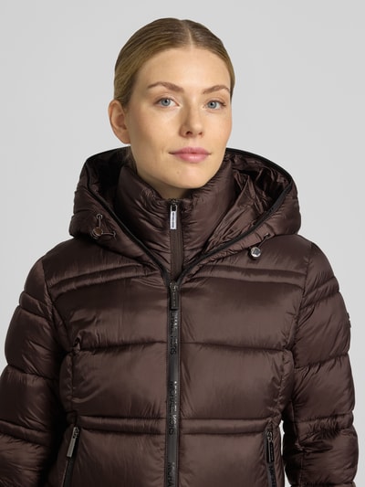 Frauenmodel trägt Steppjacke mit Kapuze und Reißverschlusstaschen von MICHAEL Michael Kors in Dunkelbraun, glänzende Oberfläche, Struktur durch Steppnähte, sichtbare Reißverschlüsse, gerader Schnitt, Nahaufnahme Oberkörper.
