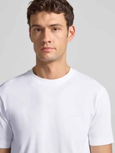 Männermodel draagt T-Shirt uit katoen model 'Thompson' van BOSS, rechte pasvorm, wit, subtiel logo, ronde hals, close-up bovenlichaam.