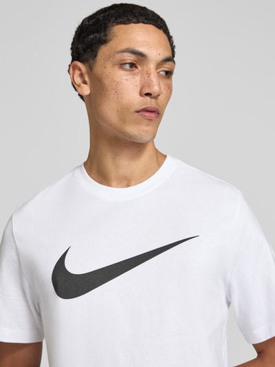 Männermodel trägt Regular Fit T-Shirt aus reiner Baumwolle von Nike, weiß mit schwarzem Logo, Nahaufnahme Oberkörper.
