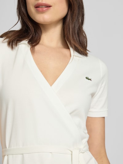 Kobiece modelka nosi Slim Fit Wickelkleid aus Baumwoll-Mix von Lacoste, efekt: jednolity kolor, dekolt w serek, wyhaftowane logo, taśma do wiązania, krótki rękaw, wykończenie materiału: pika, mieszanka bawełny, zbliżenie na górną część ciała
