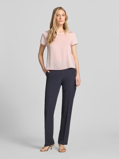 Frauenmodel trägt Blusenshirt mit Rundhalsausschnitt und abgerundetem Saum von Rinascimento im Material-Mix mit Stretch-Anteil, Loose-Fit, Rückenlänge 52 cm in Größe S, hellrosa, glatte Textur, Ganzkörperansicht von vorne.