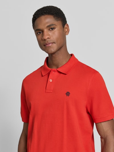Männermodel trägt Slim Fit Poloshirt mit Label-Stitching von MCNEAL aus reiner Baumwolle, rote Farbe, Knopfleiste, Nahaufnahme Oberkörper. Rückenlänge bei Größe M: 72 cm.