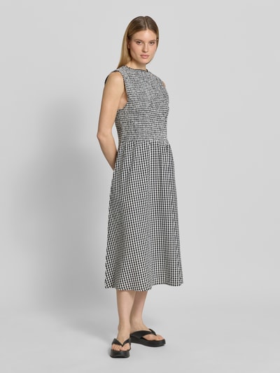 Frauenmodel trägt Midikleid mit Smok-Details und Eingrifftaschen von 7578268 aus Reine Baumwolle, A-Linie, kariertes Muster, Ganzkörperansicht von vorne.