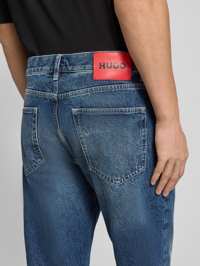 Męski model nosi Relaxed Fit Jeans aus reiner Baumwolle Modell 'HUGO 838' od HUGO, niebieski denim, widok z tyłu, zbliżenie na kieszenie i naszywkę.