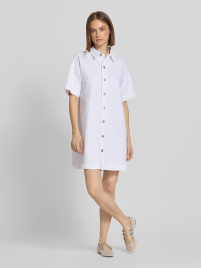 Frauenmodel trägt Loose Fit Jeanskleid aus Baumwoll-Mix Modell 'SKY' von Pieces in Weiß mit Knopfleiste, Mini-Länge, Ganzkörperansicht von vorne.