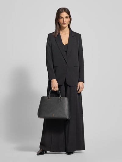 Vrouwenmodel draagt Handtasche mit Logo-Applikation Modell 'HANNA' van Lauren Ralph Lauren, zwart, gestructureerd oppervlak, voorkant volledig zichtbaar, Ganzkörperansicht von vorne. Context: Dameshandtas van Lauren Ralph Lauren, open hoofdvak, draaghengsel, binnenvak met ritssluiting, breedte 34 cm, lengte 27 cm, diepte 16 cm, schouderriem 81 cm.