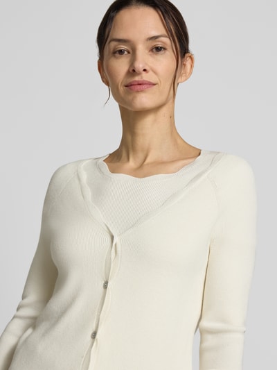 Frauenmodel trägt Strickcardigan aus Viskose-Mix von Christian Berg Woman in Creme mit Rüschen und Knopfleiste, Nahaufnahme Oberkörper.