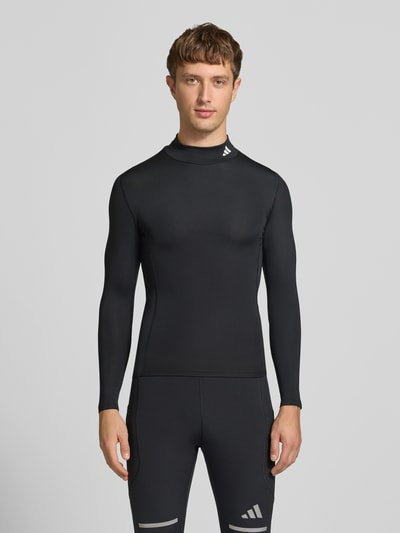 Männermodel trägt schwarzes Sport-Langarmshirt mit Mock-Neck von adidas, glatte Textur, schlichtes Design, adidas Training, Ganzkörperansicht von vorne