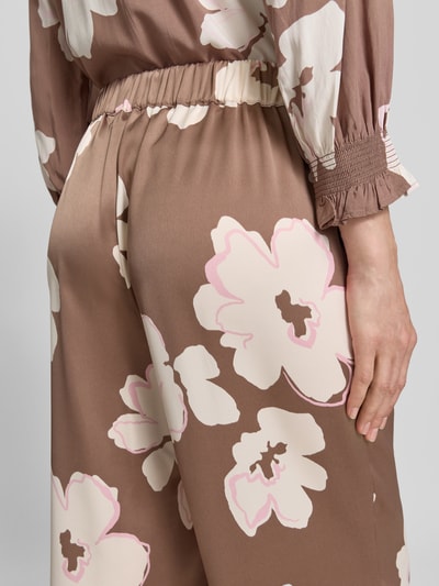 Frauenmodel trägt Loose Fit Satinhose mit Allover-Muster von s.Oliver BLACK LABEL, braun mit floralen, abstrakten Mustern, Materialverarbeitung: Satin, elastischer Bundabschluss, seitliche Eingrifftaschen, Nahaufnahme Hüfte und Oberschenkel.