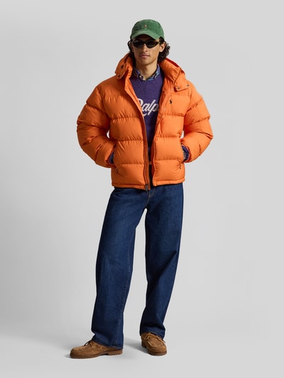 Männermodel trägt orange Steppjacke mit Zweiwege-Reißverschluss von POLO RALPH LAUREN aus Polyester, Kapuze, unifarben, Ganzkörperansicht von vorne.
