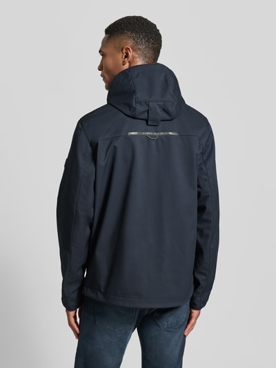 Männermodel trägt Jacke mit Reißverschlusstaschen von camel active in Dunkelblau mit Kapuze und Statement-Stitching, Ganzkörperansicht Rückansicht.