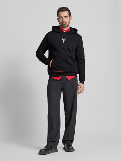 Männermodel trägt Hoodie mit Kapuze von CARLO COLUCCI in Schwarz mit Label-Print, Känguru-Tasche, Baumwoll-Mix, Lockerer-Schnitt, Ganzkörperansicht von vorne.