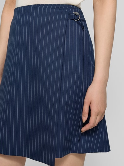 Frauenmodel trägt Leicht ausgestellter Mini-Rock in Wickeloptik Modell 'RABISU' von HUGO, dunkelblau mit Nadelstreifen-Muster, Twill, Bindegürtel, Reißverschluss, Optik:Allover-Muster, asymmetrischer Saum, Nahaufnahme Oberkörper.