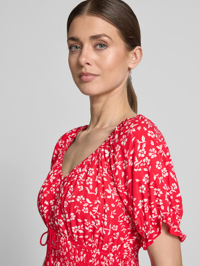 Kobiece modelka nosi Minikleid aus Viskose mit Quasten und Smok-Details od Apricot, czerwona sukienka z białym kwiatowym wzorem, taliowany krój, dekolt V, rękawy z falbankami, ściągacz w talii, troczki z frędzlami, dół z falbaną, długość pleców w rozmiarze S: 81 cm, szerokość w rozmiarze S: 35 cm, długość rękawa w rozmiarze S: 22 cm, zbliżenie na górną część ciała z przodu