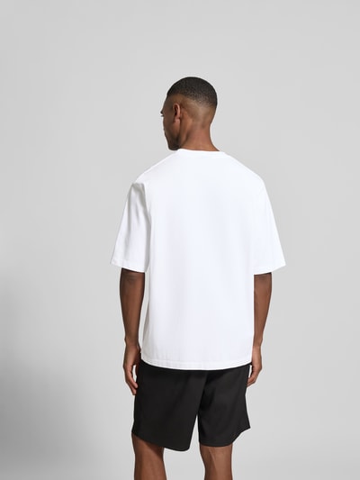 Männermodel trägt Loose Fit T-Shirt aus reiner Baumwolle von Dsquared2 in Weiß mit Label-Stitching, Rückseite verlängert, Ganzkörperansicht Rückansicht.