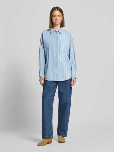 Modelka kobieca nosi Oversized Jeansbluse mit Brusttasche Modell 'KATRI' od Noisy May, jasnoniebieski kolor, czysta bawełna, luźny krój, koszulowy kołnierz, listwa guzikowa, kieszeń na piersi, obniżone ramiona, sportowe mankiety, zaokrąglony dół, długość tyłu S: 72 cm, długość rękawa S: 50 cm, przód, widok całej sylwetki.