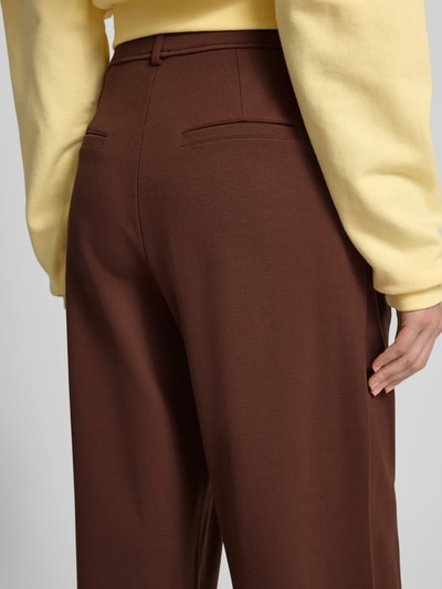 Frauenmodel trägt Wide Fit Stoffhose aus Viskose-Mix Modell 'Miri' von OH APRIL in Braun mit Bundfalten und Gesäßtaschen, Nahaufnahme Rückansicht.