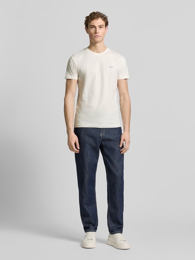 Männermodel trägt T-Shirt mit Label-Detail von Gant aus reiner Baumwolle, gerader Schnitt, Rundhalsausschnitt, cremefarben, Ganzkörperansicht von vorne.