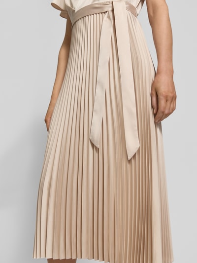 Frauenmodel trägt Midikleid mit Plisseefalten und V-Ausschnitt von comma, beigefarbener Stoff mit Bindegürtel, Nahaufnahme Oberkörper bis Knie. Material-Mix mit Stretch-Anteil und tailliertem Schnitt.