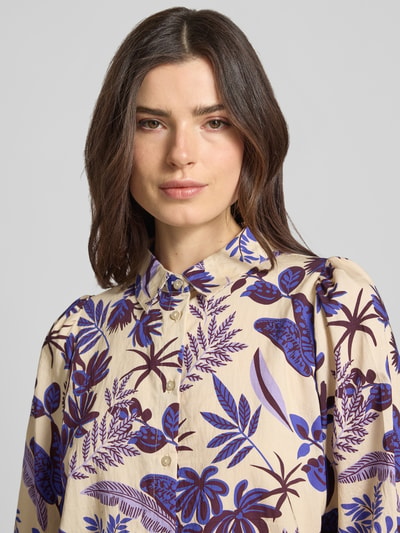 Modelka kobieca nosi Boxy Fit Bluse im Allover-Look Modell 'Bono' od LOLLYS LAUNDRY z mieszanki wiskozy, kremowe tło z fioletowym i niebieskim botanicznym wzorem, kołnierz koszulowy, kontekst: damska bluzka LOLLYS LAUNDRY, krój boxy fit, długość pleców dla rozmiaru S: 59 cm, długość rękawa S: 44 cm, zbliżenie na górną część ciała
