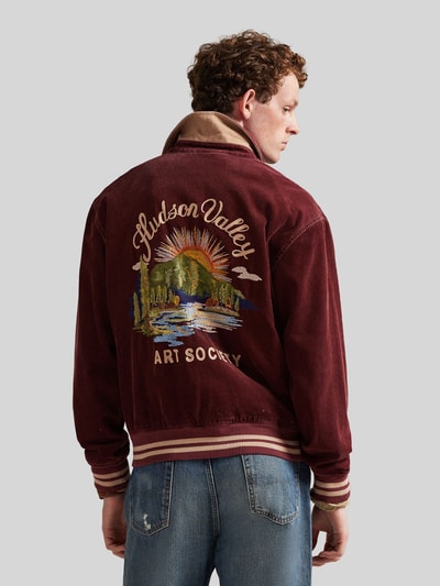 Mężczyzna nosi Regular Fit Blouson aus Baumwoll-Cord von Polo Ralph Lauren w kolorze bordowym, faktura sztruksowa, gładki wzór, haft, widok całej sylwetki z tyłu.