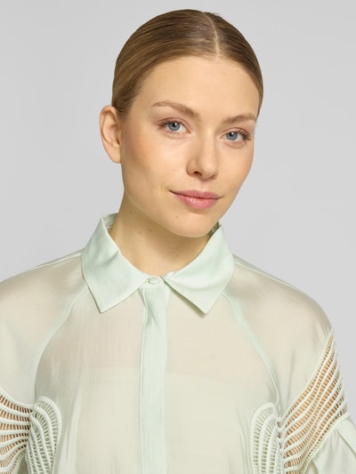 Vrouwenmodel draagt Regular Fit blouse met overhemdkraag, model 'MOLLY' van Copenhagen Muse, verdekte knoopsluiting, ruglengte maat S 67 cm, mouwlengte maat S 76 cm, lichtgroene kleur, transparante stof, zachte textuur, detailopname bovenlichaam.