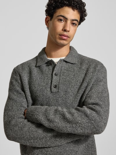Männermodel trägt Strickpullover aus Woll-Mix mit Polokragen von Calvin Klein Jeans in Grau mit Knopfleiste, Label-Detail, Nahaufnahme Oberkörper. Regular-Fit, Rückenlänge 76 cm, Ärmellänge 72 cm, Größe M.