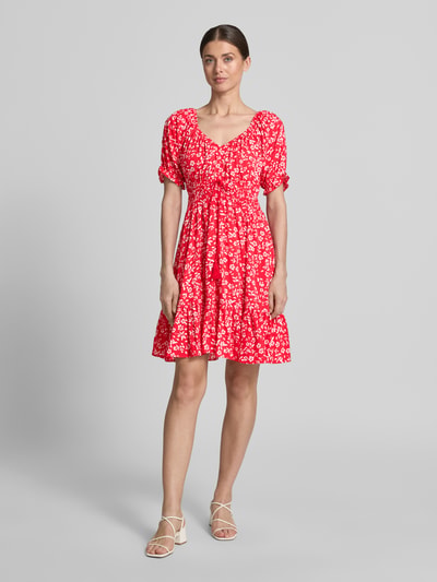 Modelka kobieca nosi Minikleid aus Viskose mit Quasten und Smok-Details od Apricot, czerwony, wzór kwiatowy, krój taliowany, dekolt V, rękawy z falbanami, sznurek z chwostami, szerokość w rozmiarze S 35 cm, długość tyłu w rozmiarze S 81 cm, długość rękawa w rozmiarze S 22 cm, widok całej sylwetki z przodu.