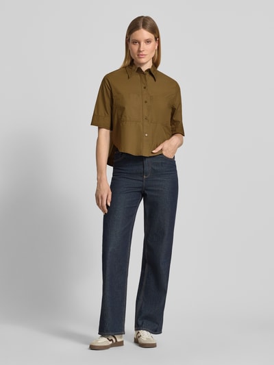 Frauenmodel trägt Boxy Fit Kurzarmbluse aus Baumwoll-Lyocell-Mix von s.Oliver RED LABEL in Olivgrün und dunkle Jeans, Ganzkörperansicht von vorne.