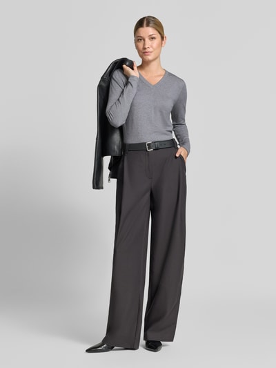 Frauenmodel trägt Pullover aus Viskose-Mix mit V-Ausschnitt von Christian Berg Woman, graue Farbe, gerader Schnitt, gerippte Abschlüsse, Kombi mit weiter schwarzer Hose, Rückenlänge 46 cm, Ärmellänge 63 cm, Ganzkörperansicht von vorne.