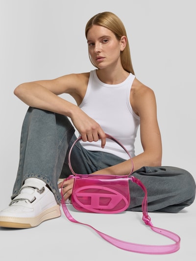 Frauenmodel trägt Shoulder Bag mit Logo-Detail von Diesel in Pink, transparenter Look, Hauptfach mit Überschlag, Nahaufnahme Oberkörper.