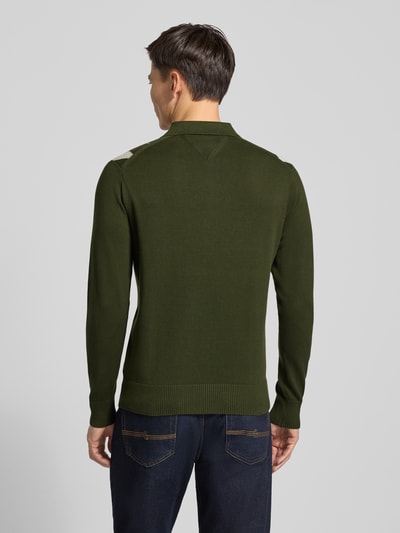 Männermodel trägt Regular Fit Strickpullover aus reiner Baumwolle von Tommy Hilfiger in Optik: Unifarben mit Gitterkaro, Gitterkaro-Muster, Label-Stitching-Applikation, Polokragen, Langarm, geripptem Rumpfabschluss und Ärmeln, Materialverarbeitung: Strick, Farbe Olivgrün, Ganzkörperansicht Rückansicht.