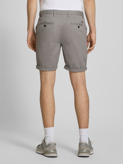 Mężczyzna nosi Regular Fit Shorts mit Münztasche od Superdry w szarym kolorze, bawełniany materiał, tylne kieszenie, szerokość w rozmiarze 32: 44 cm, długość nogawki 20 cm, widok całej sylwetki z tyłu.