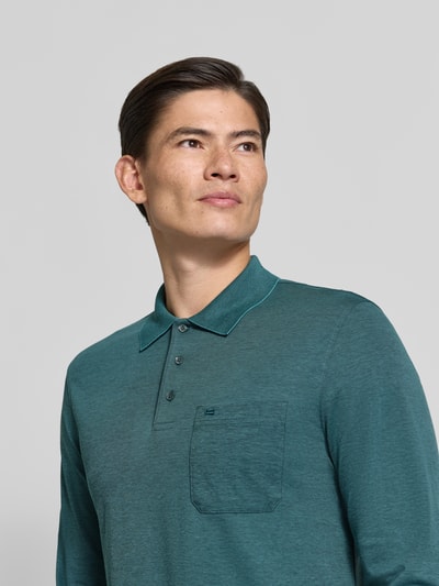 Męski model nosi Regular Fit Poloshirt mit Baumwoll-Anteil od Christian Berg Men, Mieszanka materiałów z bawełną, kołnierzyk polo, Brustasza, z długim rękawem, Długość tyłu w rozmiarze M: 70 cm, kolor zielony, prosta faktura, Nahaufnahme górnej części ciała.