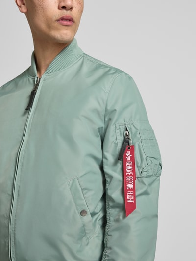 Männermodel trägt Regular Fit Jacke mit Stehkragen von Alpha Industries in Mintgrün mit Armtasche, Eingrifftaschen, Reißverschluss, elastische Abschlüsse, Nahaufnahme Oberkörper. Rückenlänge 66 cm, Schulterbreite 48 cm, Brustweite 54 cm, Ärmellänge 68 cm.