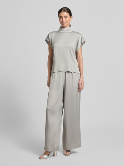 Kobiece modelka nosi Loose Fit Stoffhose mit Stretch-Anteil von Drykorn, spodnie materiałowe z mieszanki acetatu i elastanu, krój loose fit, elastyczny pas, szerokie nogawki, szerokość w rozmiarze 27/34: 35 cm, długość wewnętrzna nogawki w rozmiarze 27/34: 76 cm, jasnoszary kolor, gładka tekstura, całkowity widok z przodu.