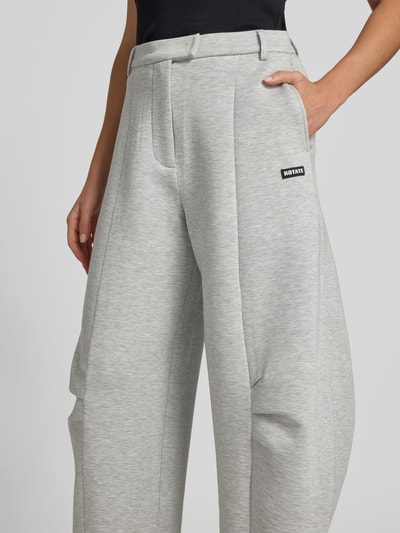 Frauenmodel trägt Hose aus Viskose-Mix von ROTATE in Grau mit Relaxed-Fit, Gelegte Falten, Logo-Patch, Haken-Reißverschluss, Nahaufnahme Oberkörper.