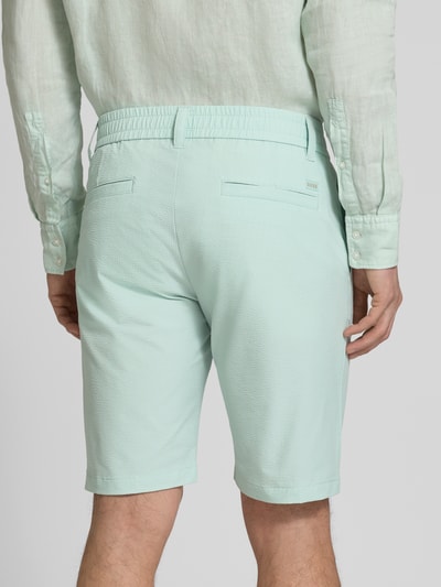 Männermodel trägt Tapered Fit Bermuda mit Kordelzug Modell 'CHINO' von BOSS Orange in Mint, Allover-Muster, Crinkle-Textur, Ganzkörperansicht Rückansicht.