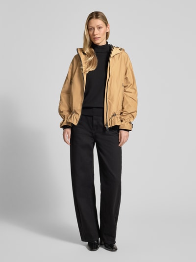Modelka nosi Kurtkę 'Jacke mit Zweiwege-Reißverschluss' od Fuchs Schmitt, krój regular fit, kaptur z tunelem, kieszenie zapinane na zamek błyskawiczny, długość tyłu w rozmiarze 36: 67 cm, szerokość ramion w rozmiarze 36: 53 cm, szerokość w klatce piersiowej w rozmiarze 36: 59 cm, długość rękawów w rozmiarze 36: 57 cm, kolor beżowy i czarny, gładka tekstura, całkowity widok z przodu.
