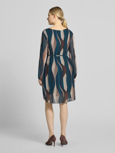 Frauenmodel trägt Knielanges Kleid mit Bindegürtel Modell 'Sa44raa' von ZABAIONE aus Chiffon, Allover-Look in Blau-Beige, Plisseefalten, Ganzkörperansicht Rückansicht.
