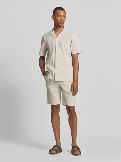 Männermodel trägt Shorts mit elastischem Bund und Strukturmuster von Lindbergh, aus Baumwoll-Mix mit Stretch-Anteil, Loose-Fit, seitliche Eingrifftaschen, in Beige mit dezenter Struktur, Bundweite 42 cm, Innenbeinlänge 25 cm, Ganzkörperansicht von vorne.