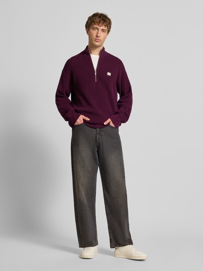 Männermodel trägt Loose Fit Troyer mit gerippten Abschlüssen von Calvin Klein Jeans in Dunkellila, Troyer-Kragen, Label-Detail, Ganzkörperansicht von vorne.